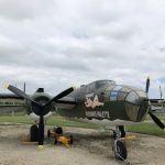 Three quarters view of the B-25 highlighting its nose art, Passionate Paulette - a white woman with brown hair lounging on the name.