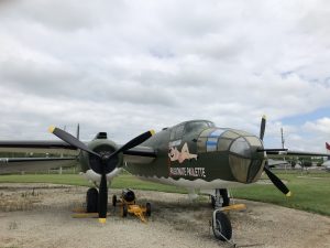Three quarters view of the B-25 highlighting its nose art, Passionate Paulette - a white woman with brown hair lounging on the name.