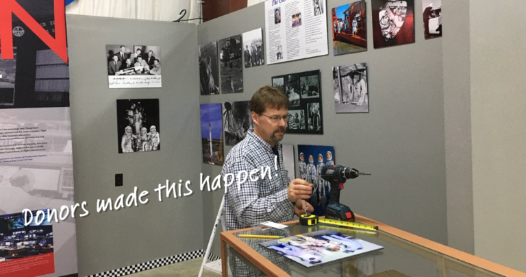 Image of a volunteer installing an exhibit on Gus Grissom with the words "Donors make this happen" overlaid