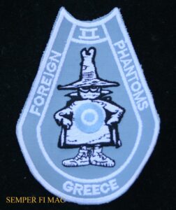 A horseshoe shaped patch in baby blue with the words "Foreign II Phantoms Greece" with a white Spooky with a blue and white target on stomach.